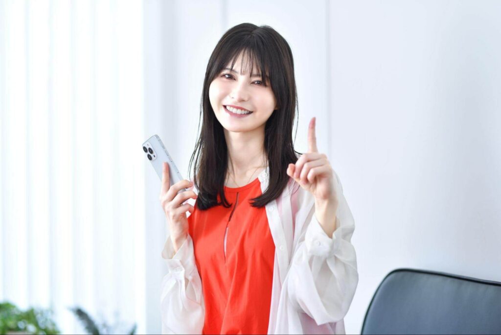 スマホを持ちながら人差し指を立てる女性