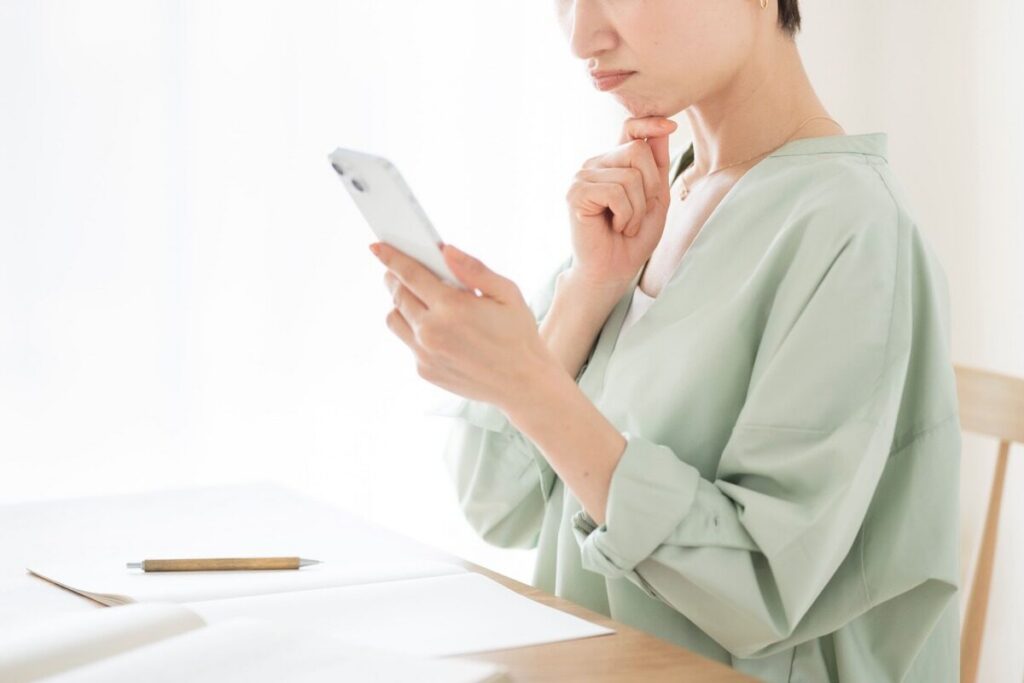 スマホを見ながら悩むグリーンの服を着た女性