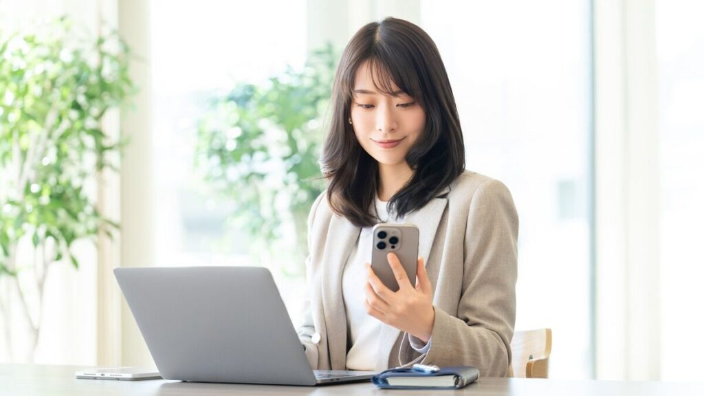 スマホを見ながらパソコンで作業する女性