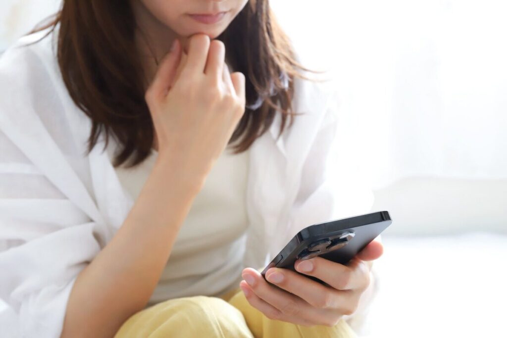 スマホを持ちながら考える白シャツの女性