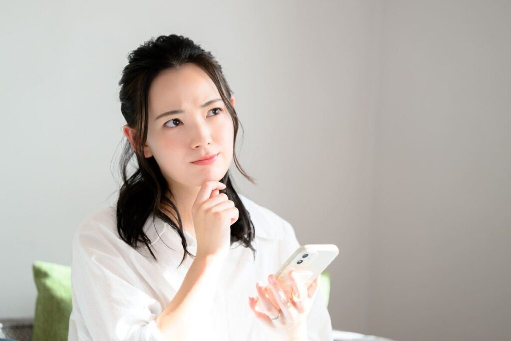 スマホを持ちながら考える女性