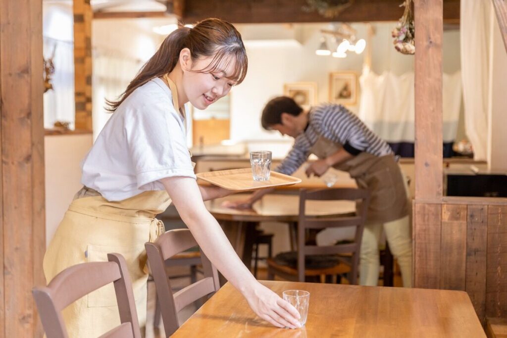 飲食店のテーブルにグラスを置く女性スタッフ